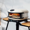 Black metal stand with wooden shelf holding black kamado-style grill with orange interior and dome lid