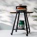 Black kamado grill on metal stand with side shelf, outdoor cooking setup