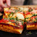 Detroit-style square pizza with crispy edges, caramelized cheese, and toppings on dark surface