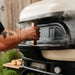 Black wood-fired pizza oven with dome design and side-mounted metal door handle, outdoor kitchen setup
