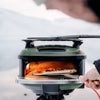Gozney Tread portable wood-fired pizza oven with olive finish, flames visible inside cooking chamber